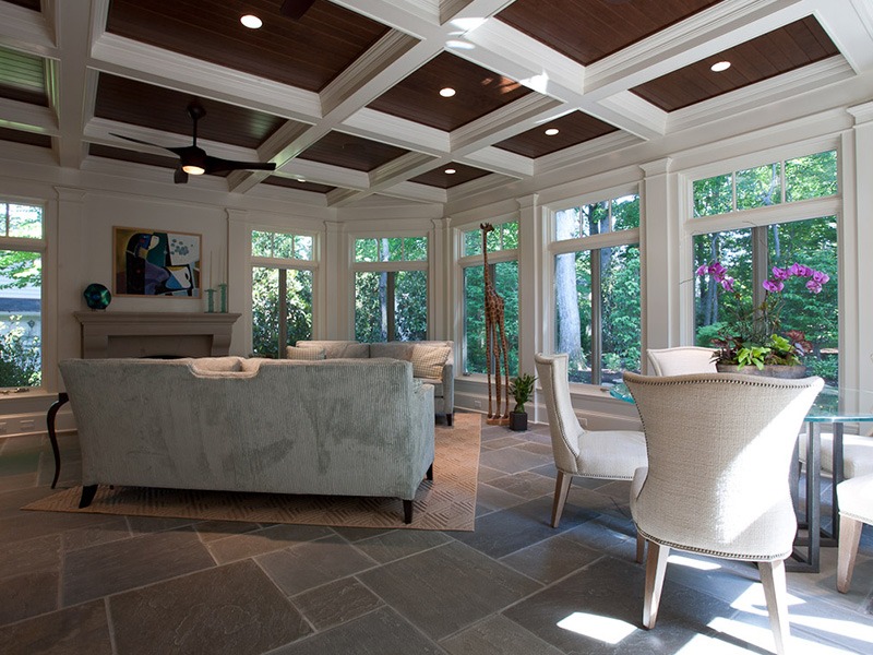Spacious sunroom with large windows, cozy sofas, a dining table, and vibrant plants. Warm light filters through, highlighting the elegant decor.